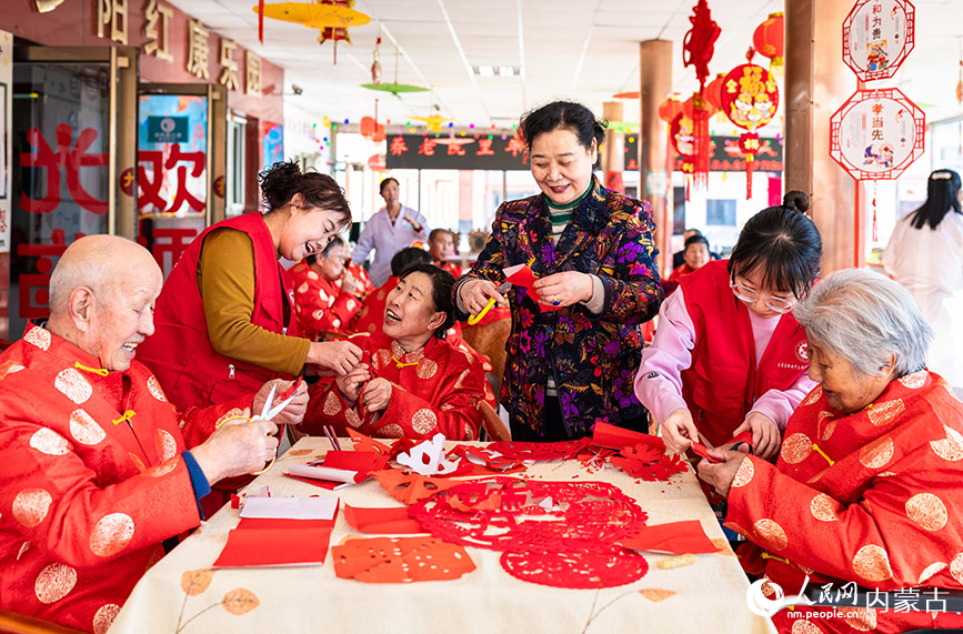 1月20日，志愿者與老人們在呼和浩特市玉泉區(qū)民政局迎新春主題活動現(xiàn)場一起剪窗花。丁根厚攝